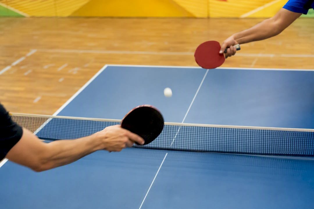 Two ping pong paddles striking ball mid-air